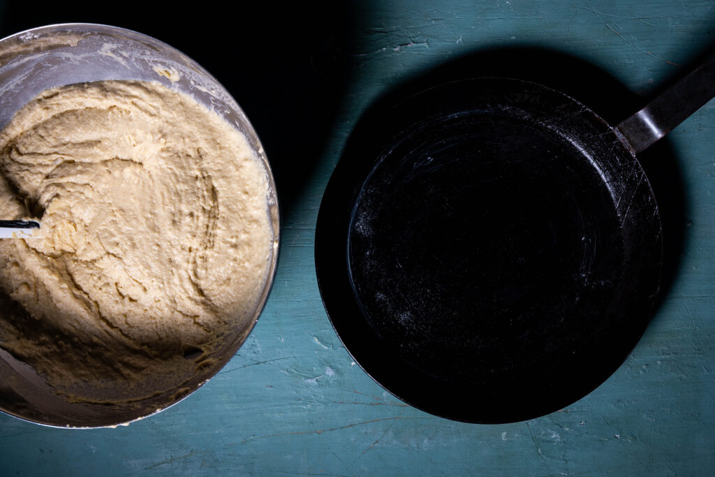 Eine eingefettete gusseiserne Pfanne und eine Schüssel mit Cornbreadteig.
