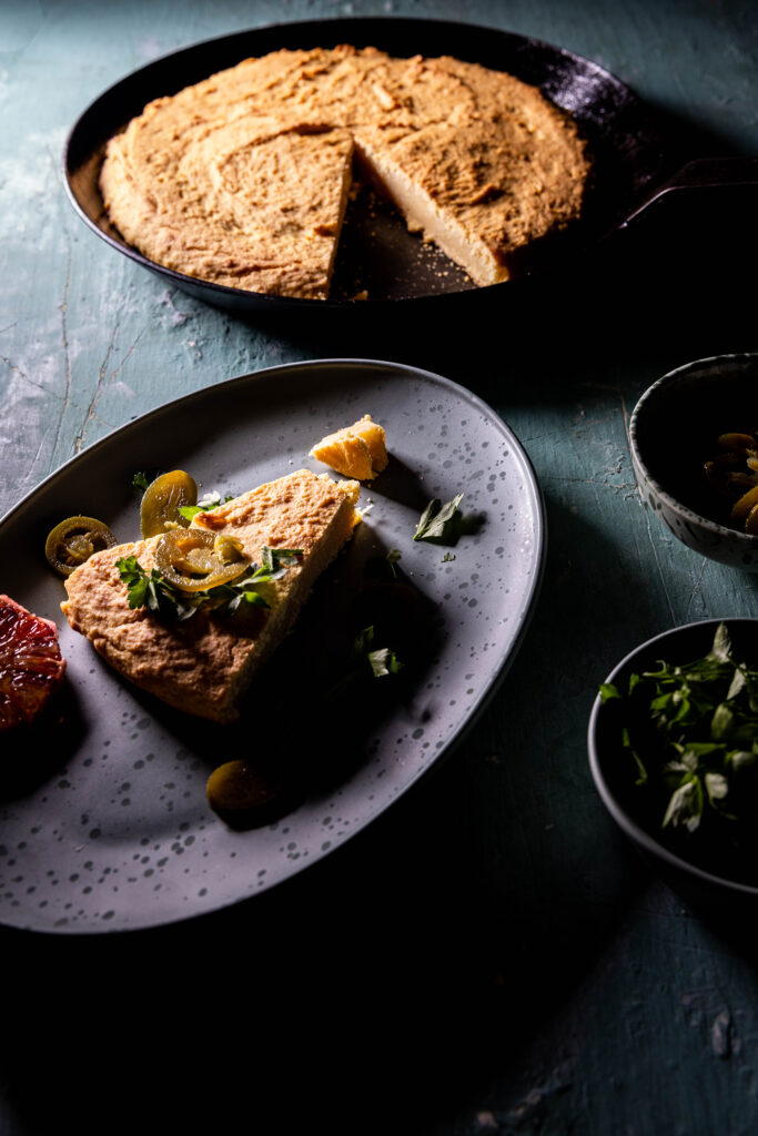 Cornbread in einer gusseisernen Pfanne, angeschnitten. Ein Stück auf einem Teller.
