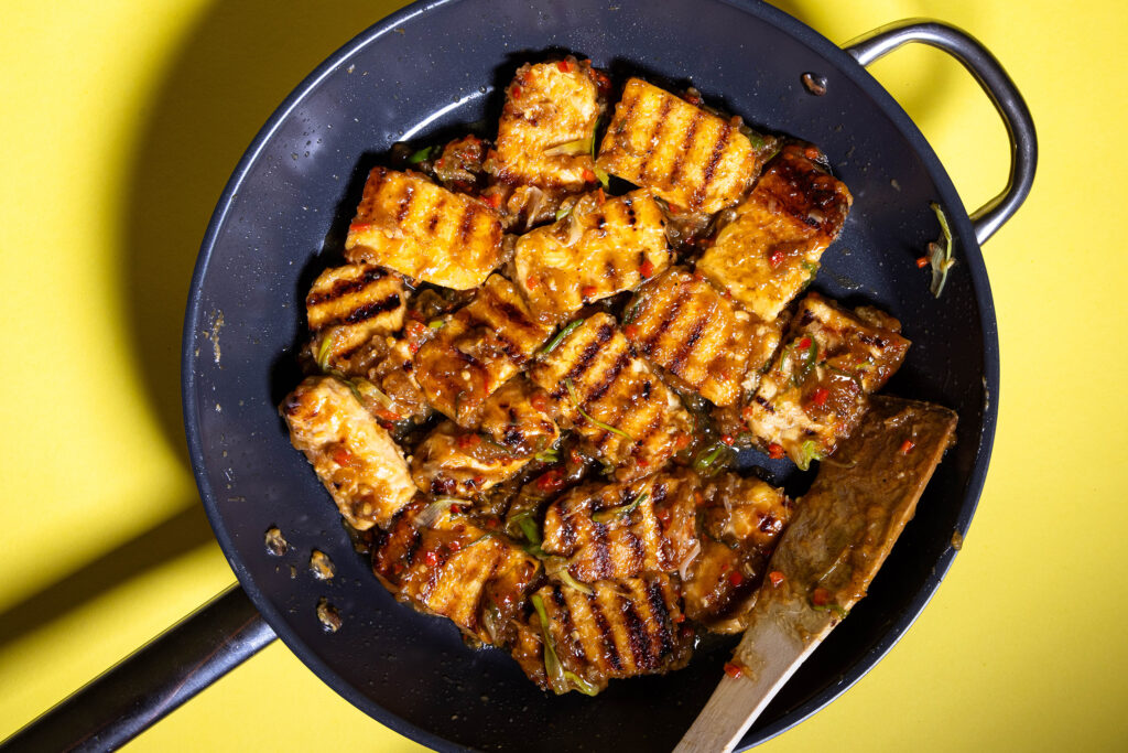 Gegrillter Tempeh brät in einer Chilisauce in einer Pfanne.