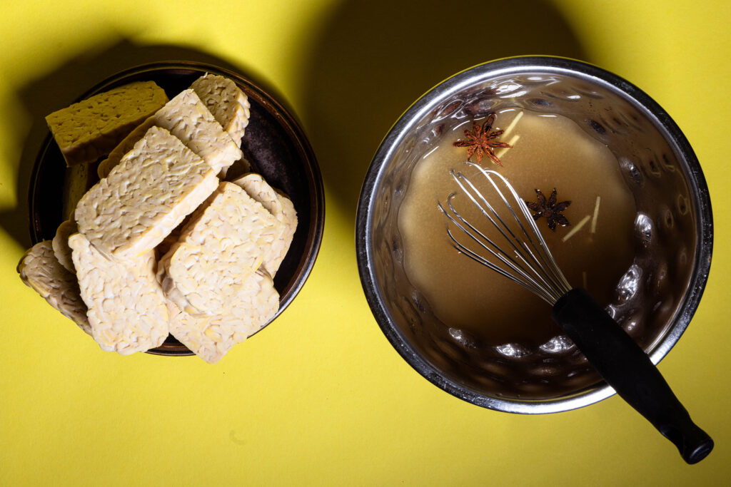 Eine Marinade für Tempeh in einer Schüssel, daneben ein Teller mit Tempehscheiben.