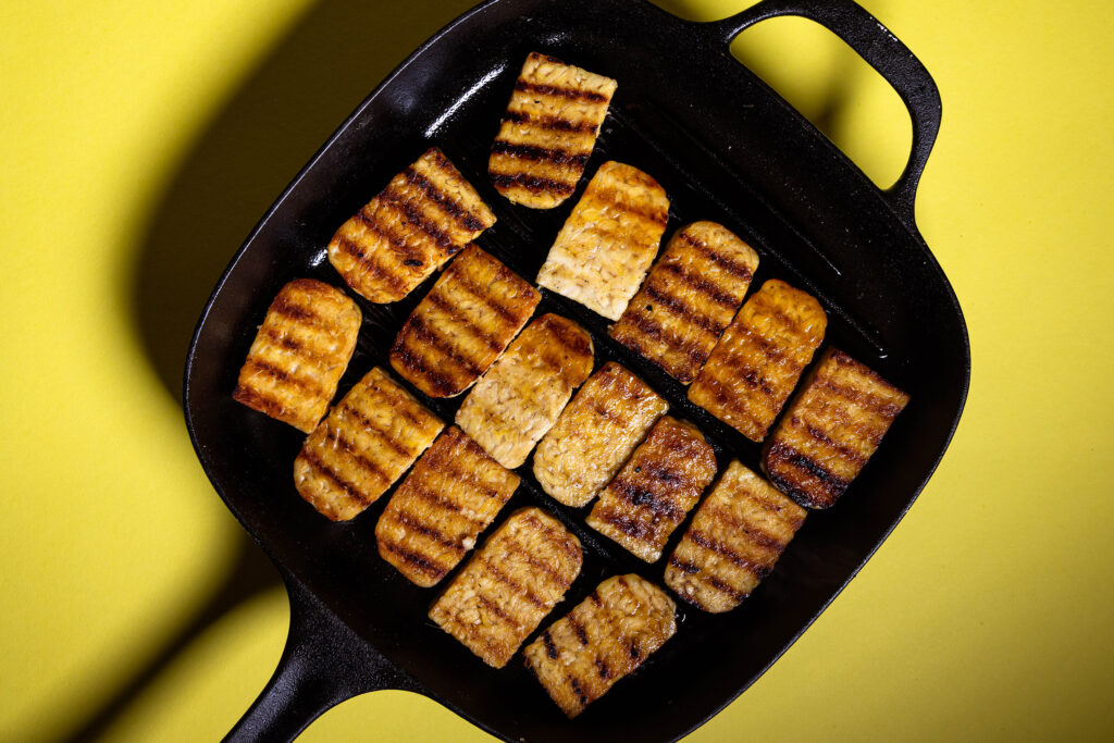 Gegrillter, mit Ahornsirup lasierter Tempeh wird in einer Grillpfanne angebraten.