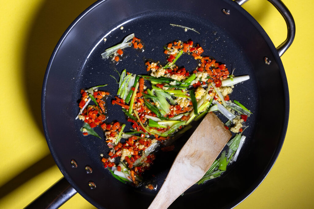 Lauchzwiebeln, gepresste Knoblauchzehen, Chili und den Ingwer braten in einer Pfanne.