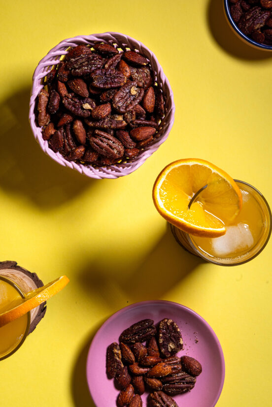 Orangen-Nüsse, in Schälchen auf gelbem Grund. Außerdem 2 Gläser Orangensaft.