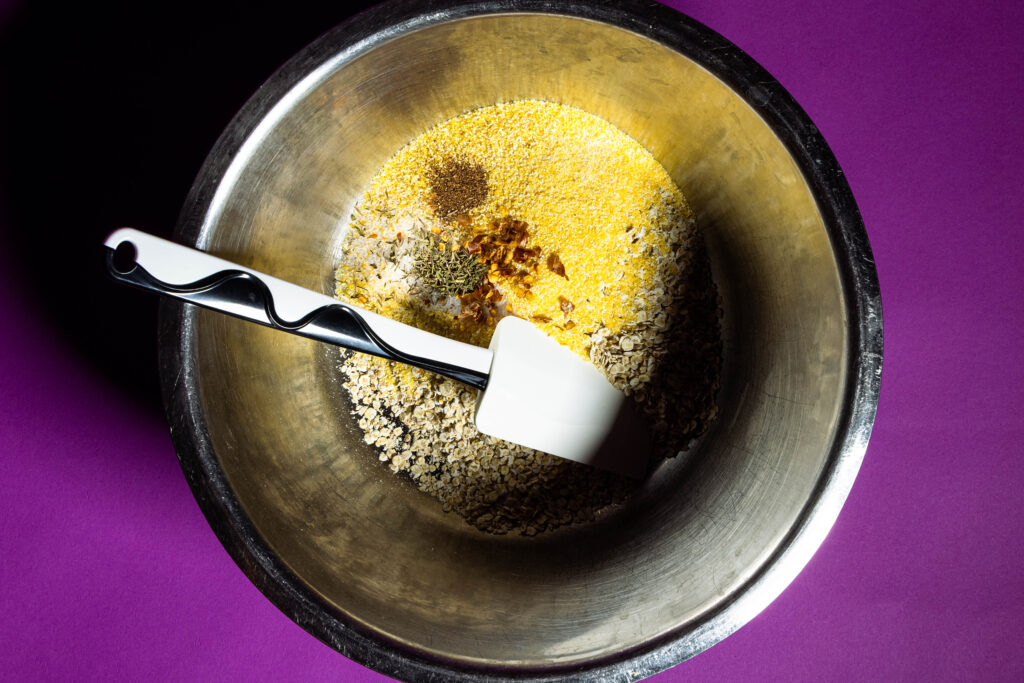 Haferflocken, Maisgrieß, Salz und Gewürze in einer Metallschüssel.