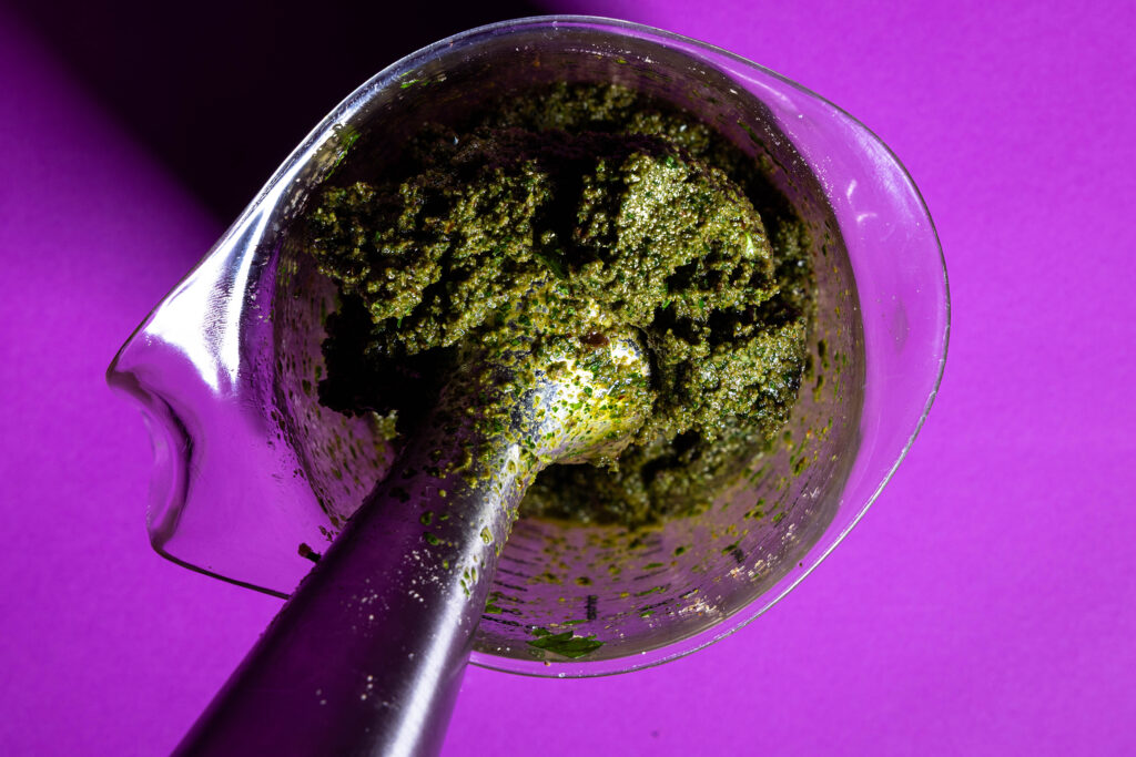 Ein grünes Pesto wird in einem Messbecher püriert.