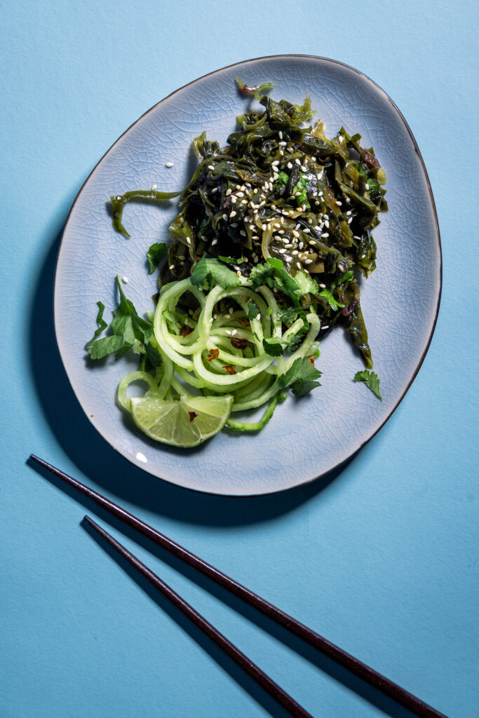 Wakame-Salat auf einem blauen Teller. Daneben Essstäbchen.