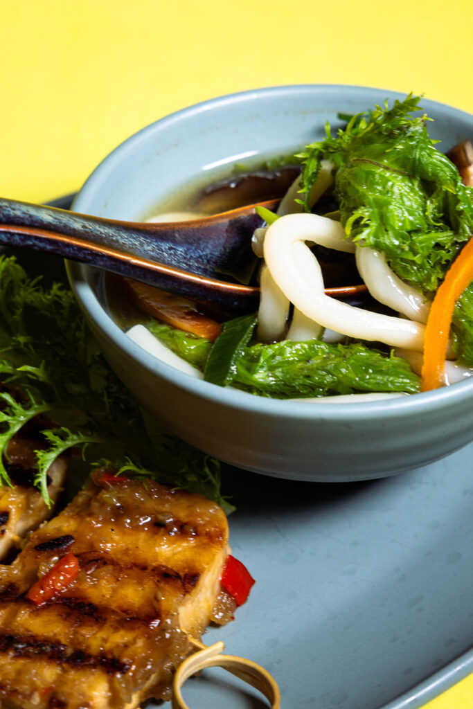 Miso-Suppe mit Wasabi-Senf-Blättern in einer Schale, aus der gerade ein Löffel genommen wird.