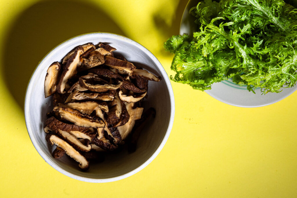 Shitake-Pilze, eingeweicht, in Scheiben geschnitten, in einer Schale, daneben ein Teller mit Wasabi-Senf