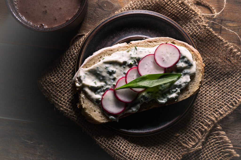 Bärlauch-Vrischkäse auf einer Scheibe Brot, mit Radieschenscheiben.