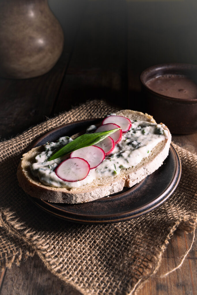 Bärlauhc-Vrischkäse mit Radieschenscheiben auf einer Scheibe Brot.
