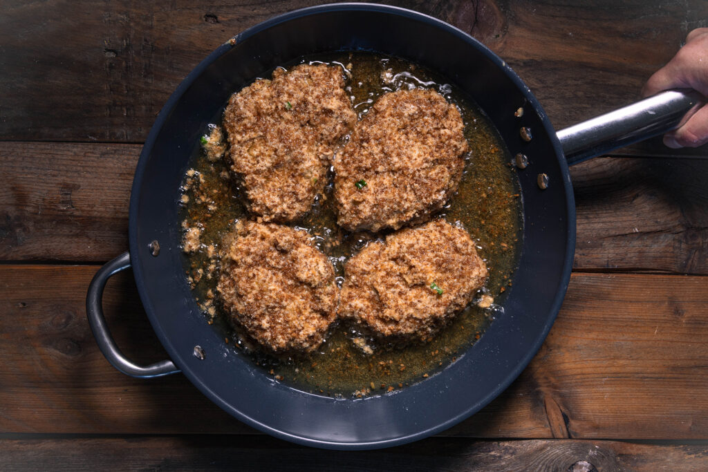 Vegane mit Bärlauch gefültle Schnitzel mit Röstzwiebelpanade braten in reichlich Öl in einer Pfanne.