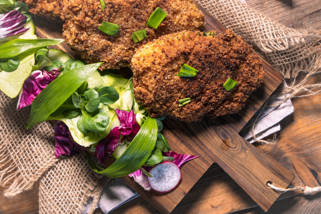 Mit Bärlauch gefülltes Schnitzel in krosser Röstzwiebelpanade auf einem Holzbrett