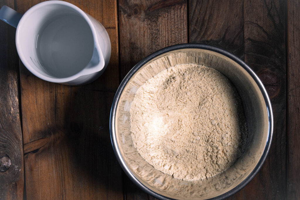 Eine trockene Seitanmischung in einer Schale und ein Krug mit Wasser