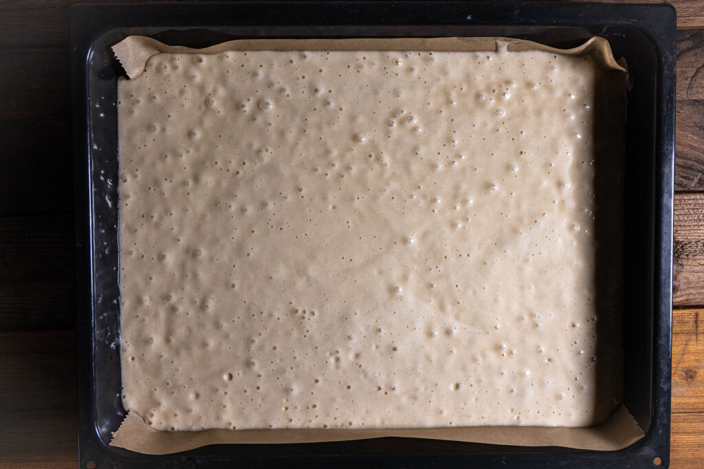 Roher, veganer Biskuitteig auf einem Blech mit Backpapier.