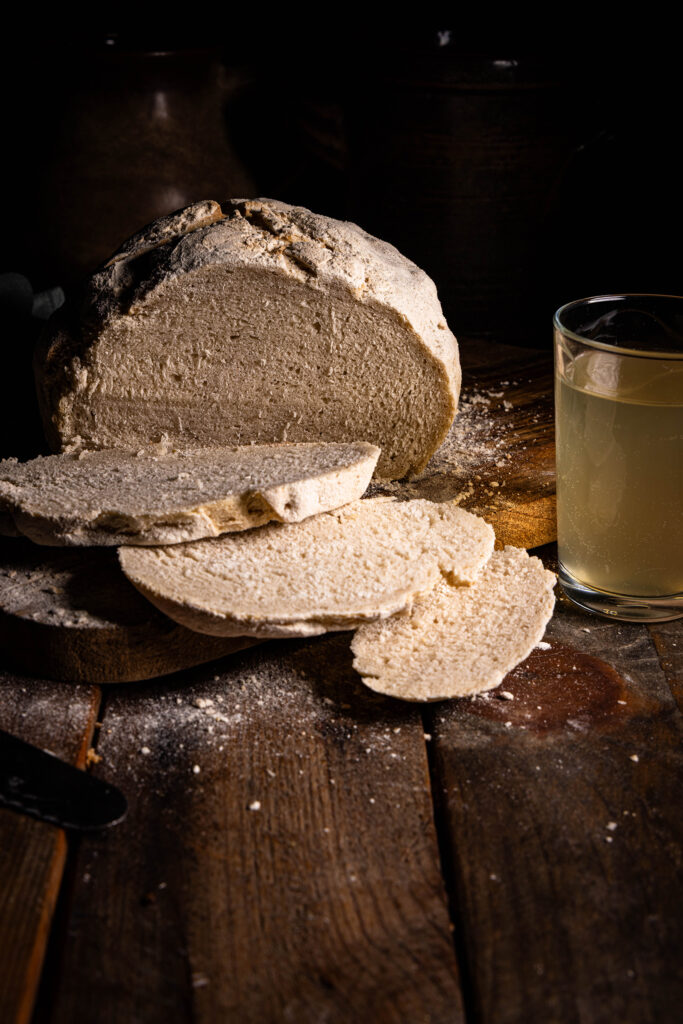 Ein Brot, gebacken mit Kefir, angeschnitten auf einem Holzbrett, daneben ein Glas Wasserkefir.