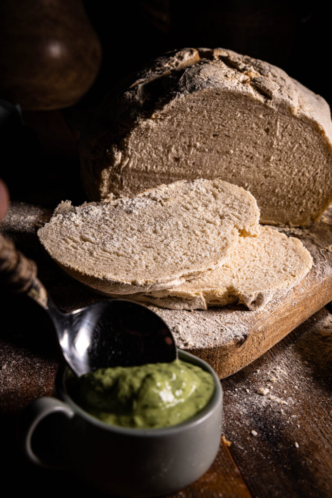 Brot, gebacken mit Wasserkefir, aufgeschnitten auf einem Holzbrett. Davor eine Schale Bärlauchaioli.