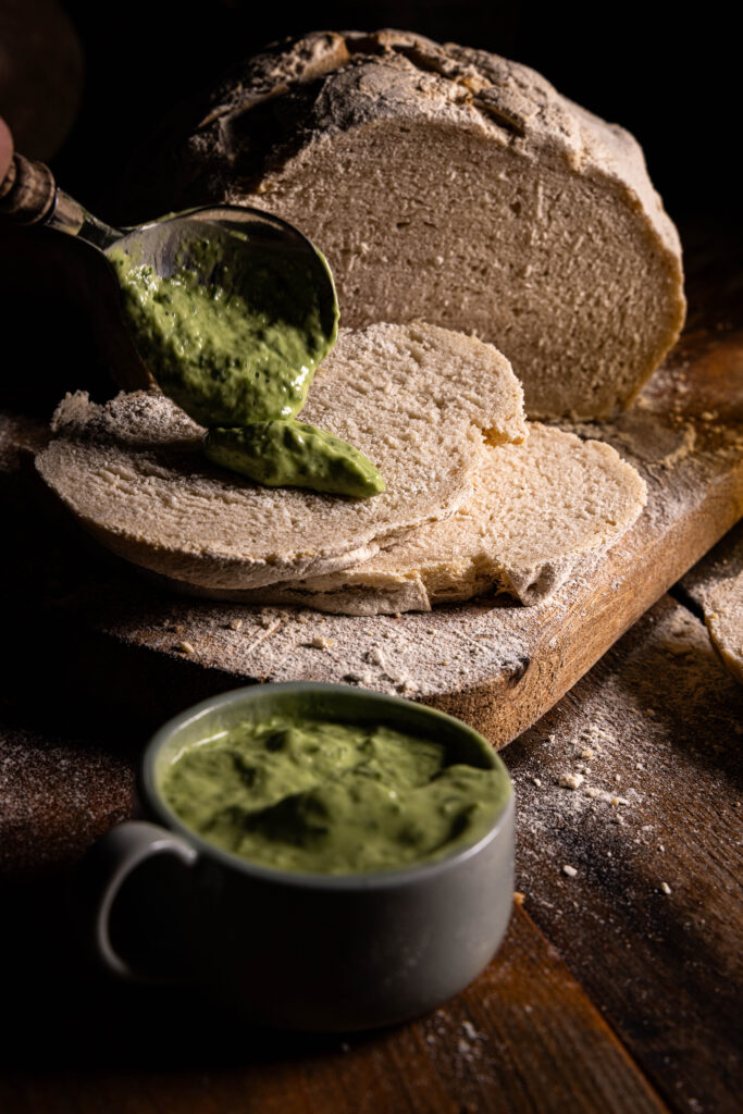Eine Scheibe Wasserkefirbrot wird mit Bärlauchaioli bestrichen.
