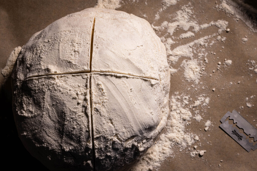 Ein ungebackenes Brot, zweimal eingeritzt, auf einem Backblech.