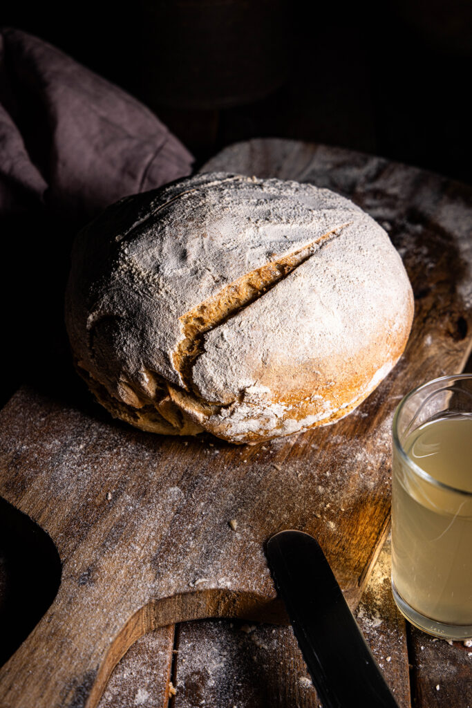 Kefir-Roggenbrot auf einem Holzbrett, daneben ein Glas Wasserkefir