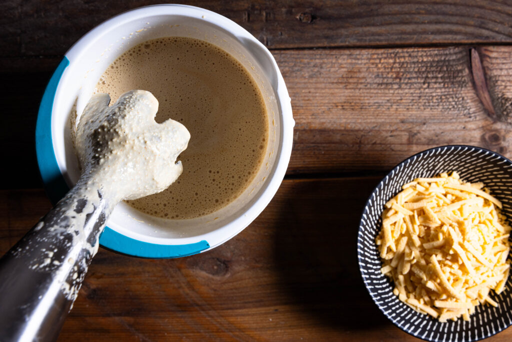 Eine vegane Käsesauce wird püriert, daneben eine Schale mit veganem Reibekäse