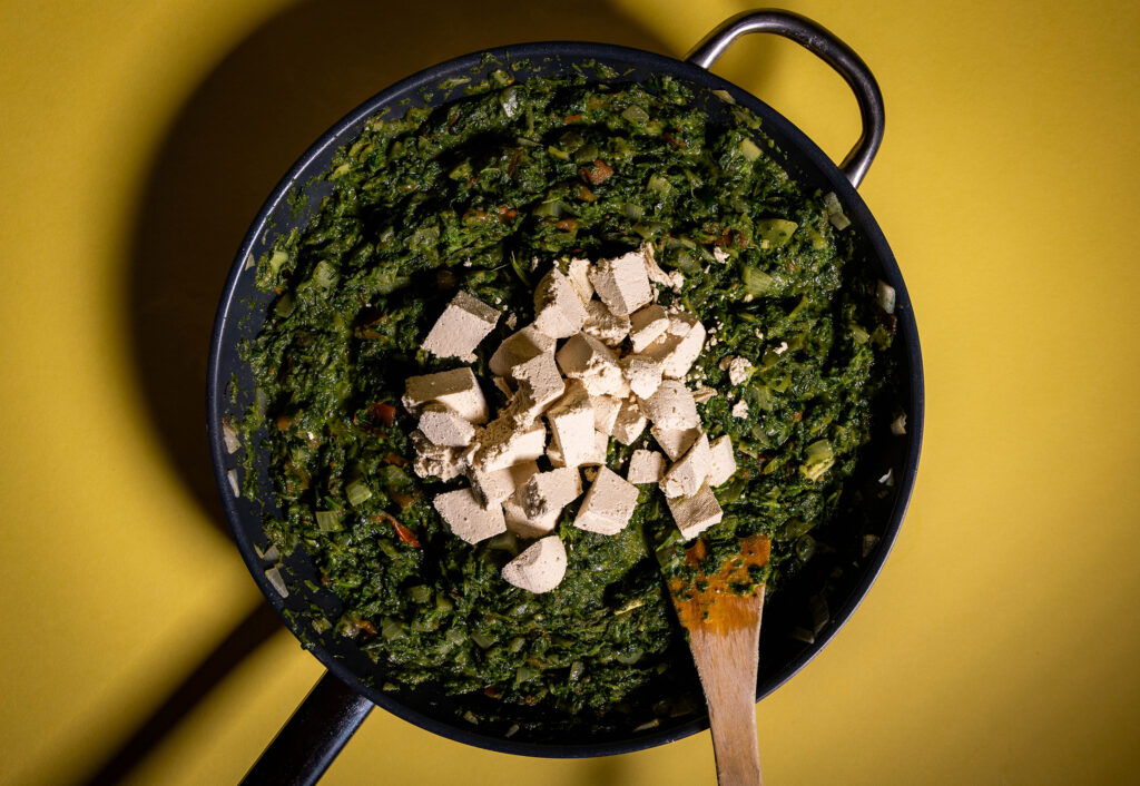 Palak Paneer in einer Pfanne, der vegane Paneer wird gerade dazu gegeben.