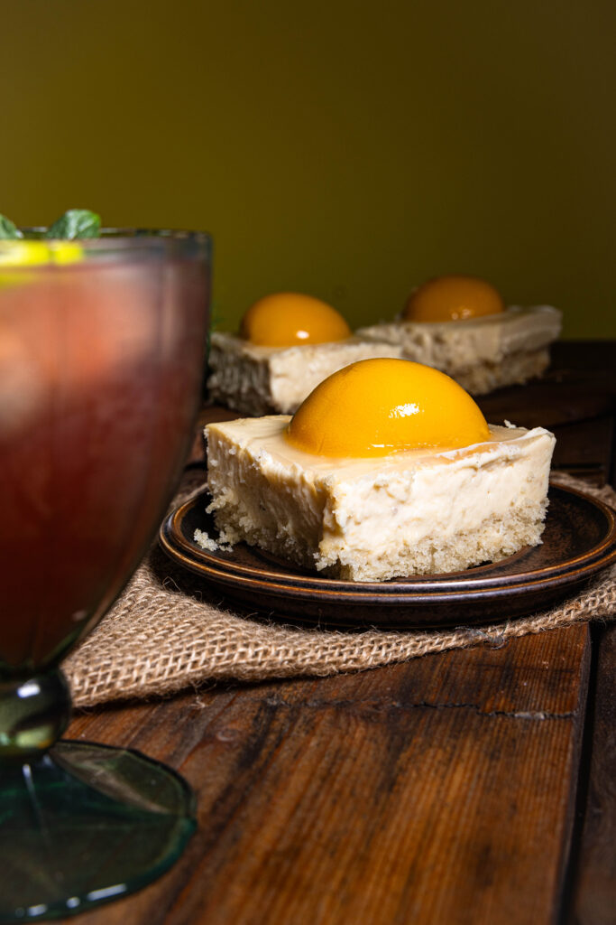 Veganer Pfirsich-Käsekuchen auf einem Teller, davor ein fancy Drink