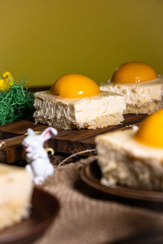 Veganer Pfirsich-Käsekuchen mit fermentierten Aprikosen auf Tellern, dazwischen Osterdeko