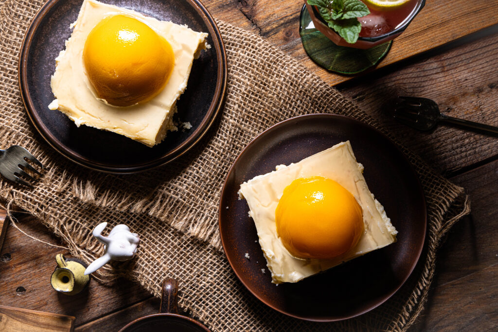 Veganer Pfirsich-Käsekuchen mit fermentierten Aprikosen - zwei Stücke auf Tellern.