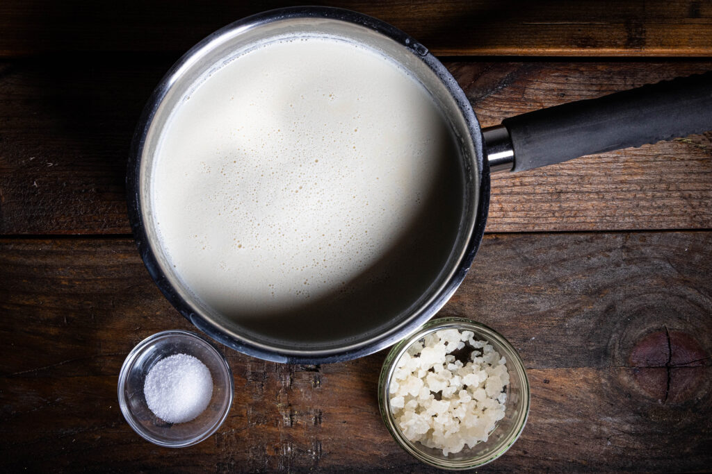 3 Zutaten auf einem Holztisch: Sojamilch, etwas Zucker und frisch abgeseihte Wasserkefirkristalle.