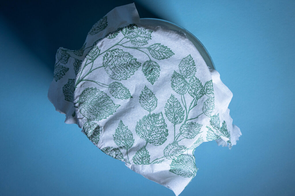 Ein Gefäß mit einem Küchentuch verschlossen.