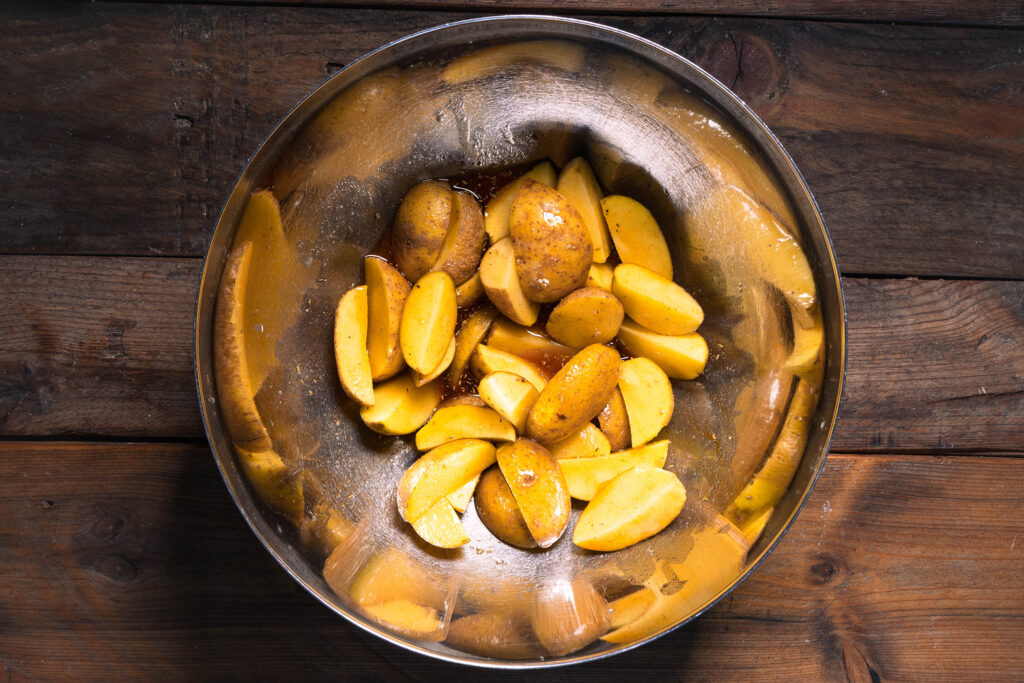 Kartoffelspalten werden in Ölmarinade gewendet.