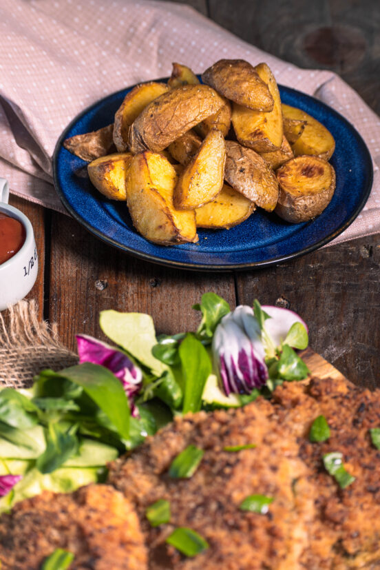 Wedges aus dem Ofen, deftig mariniert. Davor ein Teller mit Salat und veganen Schnitzeln