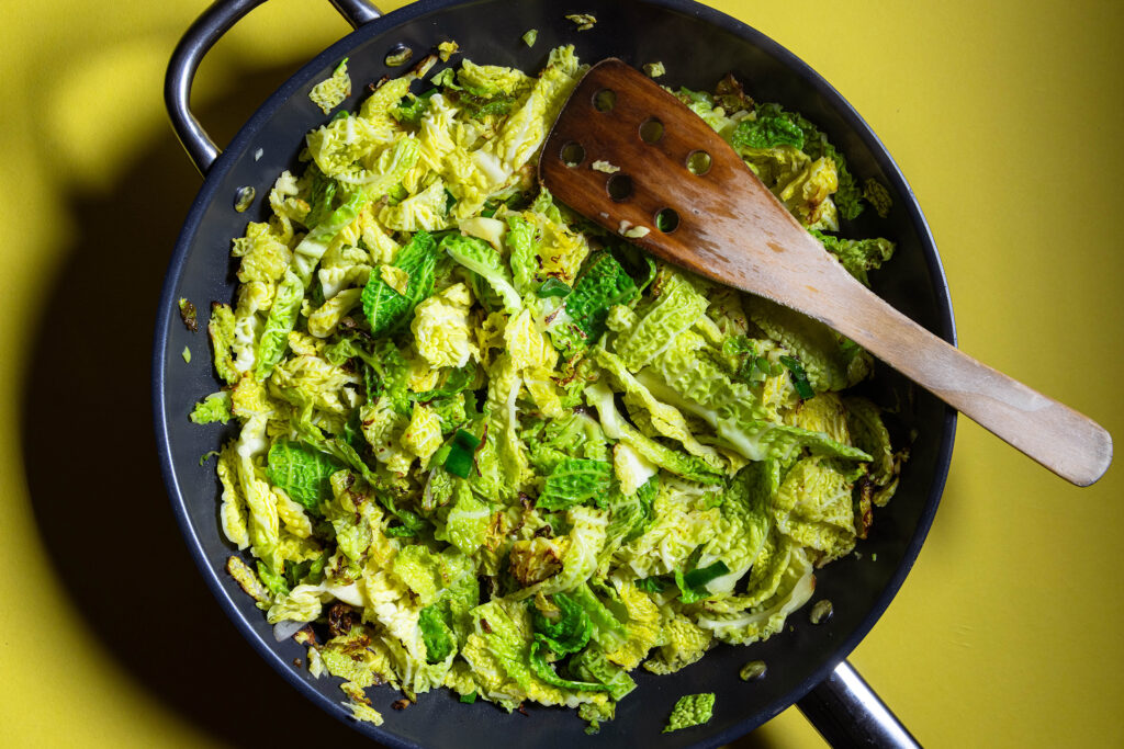 Wirsing, Schalotten und Lauchzwiebeln werden in einer Pfanne angebraten.