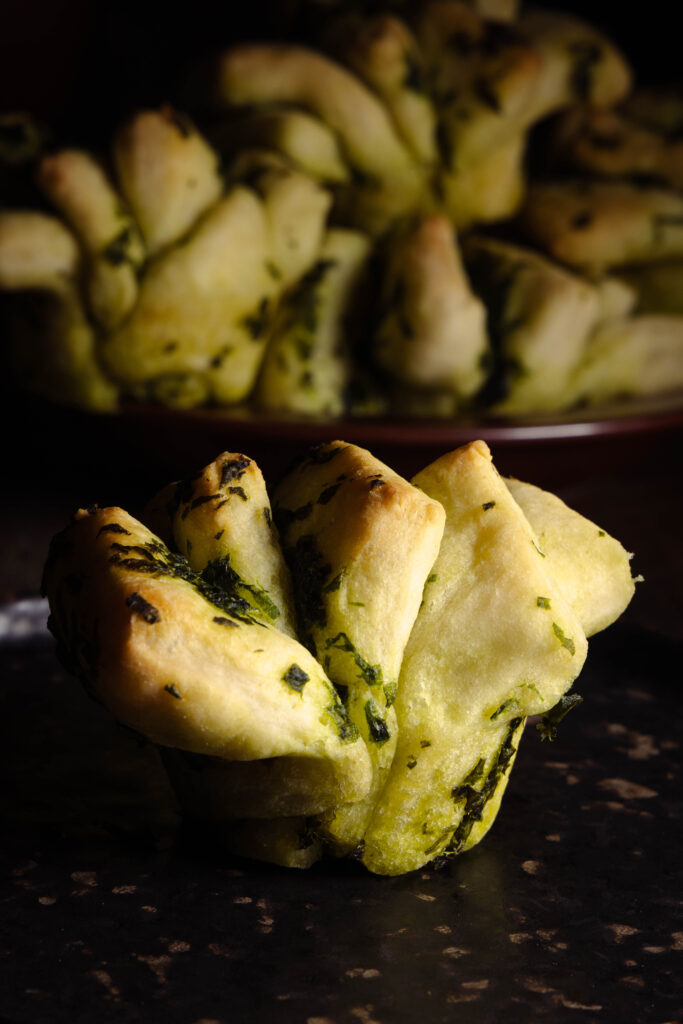Ein Bärlauch-Zupfbrot auf einem Teller, dahinter viele Bärlauch-Zupfbrote