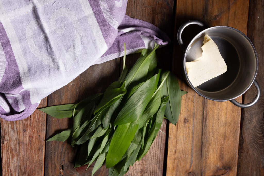 Frischer Bärlauch, vegane Butter in einem Topf und eine abgedeckte Schüssel.