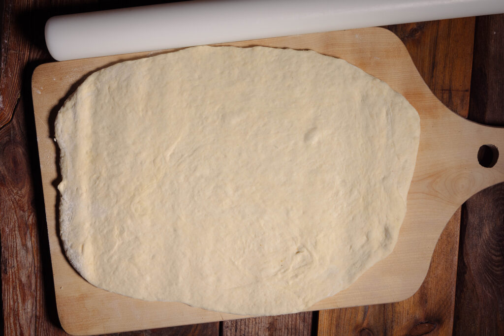 Ein Hefeteig ausgerollt auf einem großen Holzbrett.