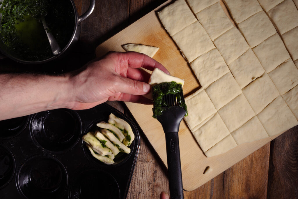 Teigrechtecke werden mit Bärlauchbutter bepinselt und in ein Muffinblech gegeben.