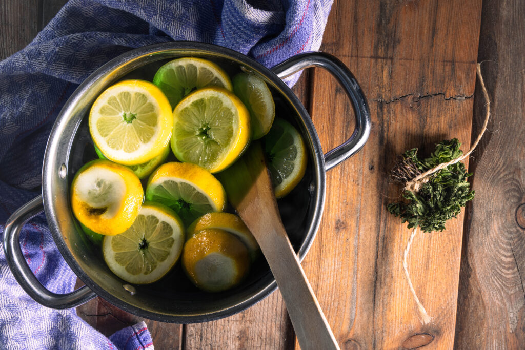 Ein Topf mit Sirup und Zitronenscheiben darin. Daneben ein welkes Bund Waldmeister.
