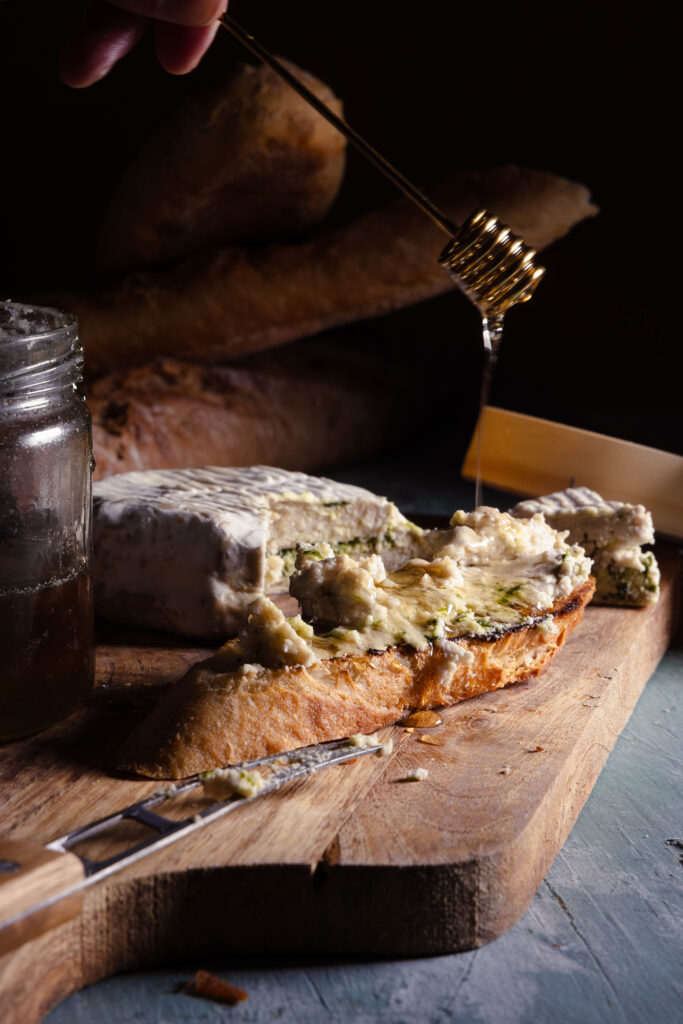 Mit Bärlauch durchzogener veganer Camembert auf einem Brot. Veganer Honig wird darüber geträufelt