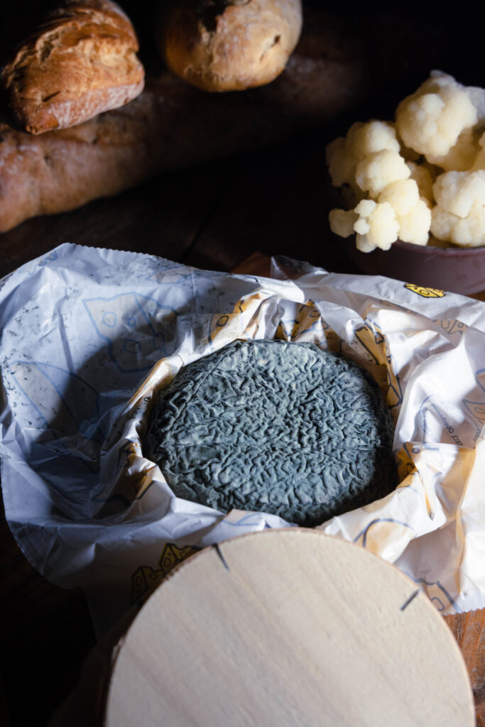 Veganer Blauschimmelkäse aus Blumenkohl in einer Holzschachtel mit Käsepapier, geöffnet, man sieht den Käse.
