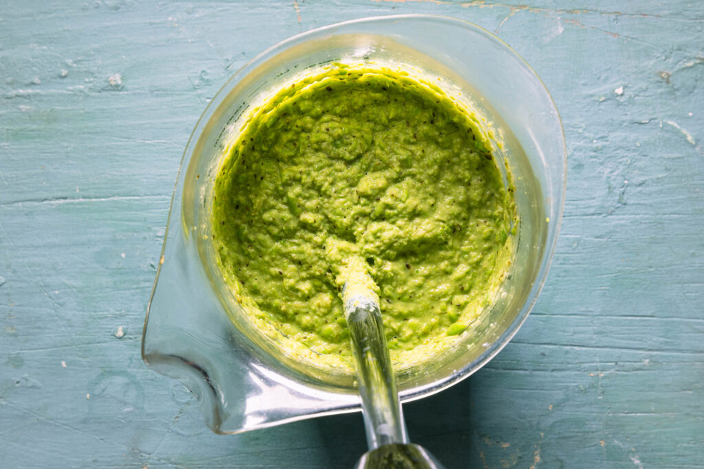 Ein grüner Dip wird in einem hohen Gefäß püriert.
