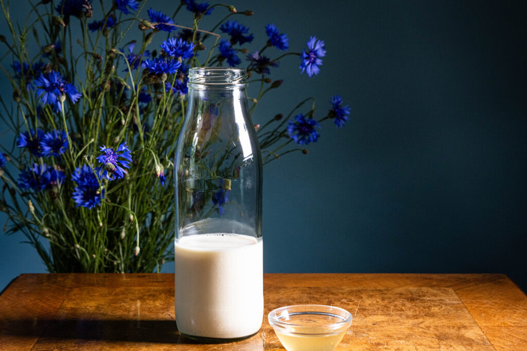 Eine Flasche mit Sojamilch und eine kleine Schale mit Apfelessig stehen auf einem antiken Tisch.