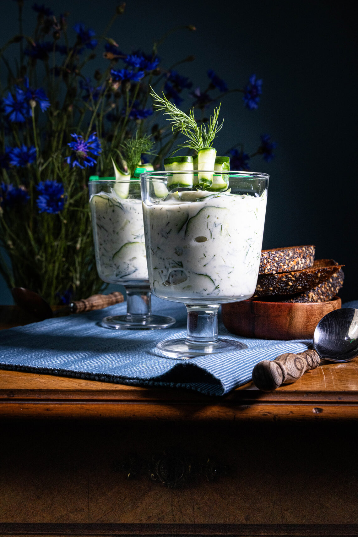 Gurkensuppe - vegan - in zwei Gläsern auf einem alten Holztisch, dahinter Kornblumen