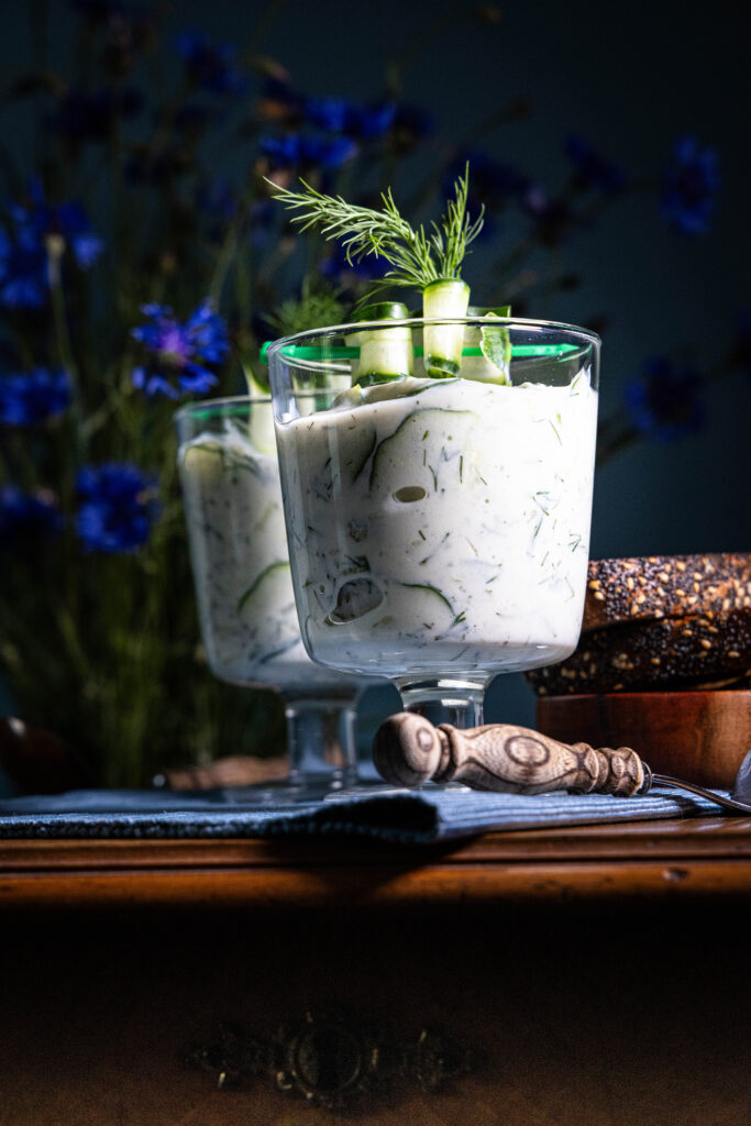Vegane Gurkensuppe in zwei Gläsern serviert. Dahinter Kornblumen.