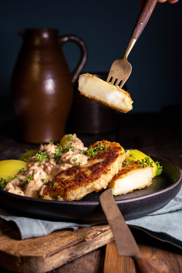 Sellerieschnitzel, vegan mit cremiger Pilz-Schinken-Sauce. Ein Stück auf einer Gabel.