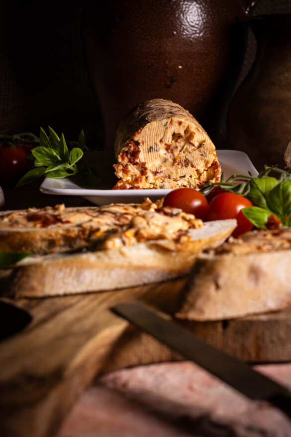Vegane Tomatenbutter - auf Baguettescheiben und als Rolle auf einem Teller.